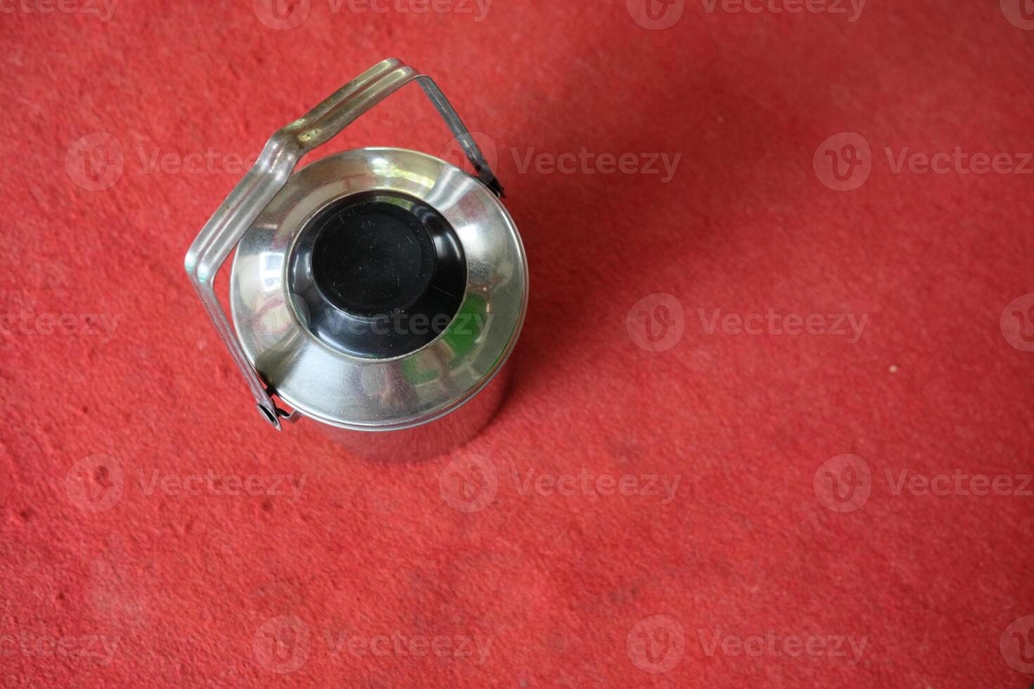 Top view of a silver metal container with a black lid and handle on a red surface. photo