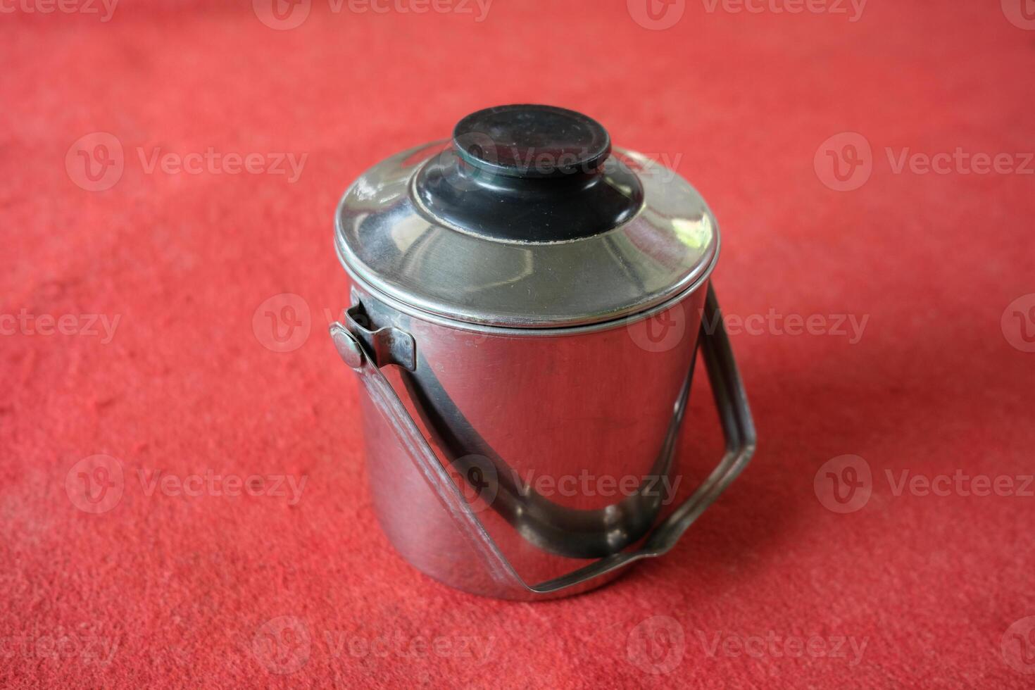 A silver container with a black lid and a handle, on a red background. photo