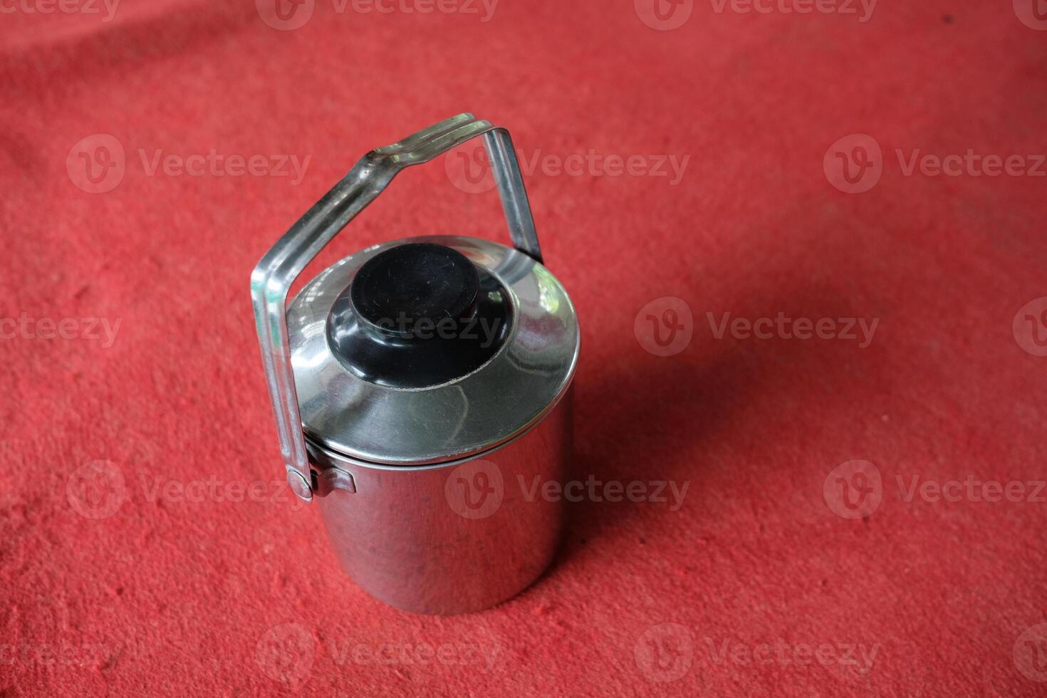 Stainless steel container with black lid and handle on red surface. photo