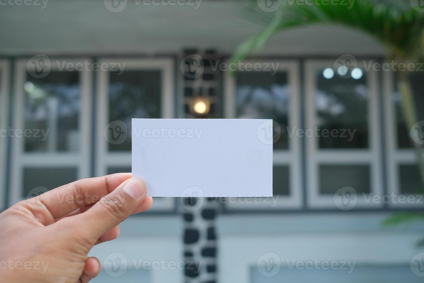 Hand holding blank white card against blurred house background. photo