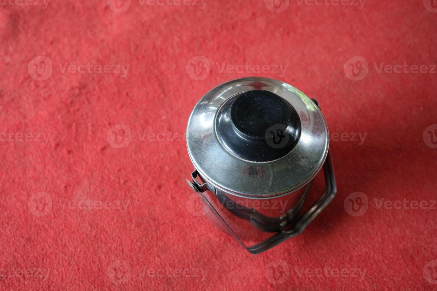 A stainless steel container with a black lid sits on a red surface. photo