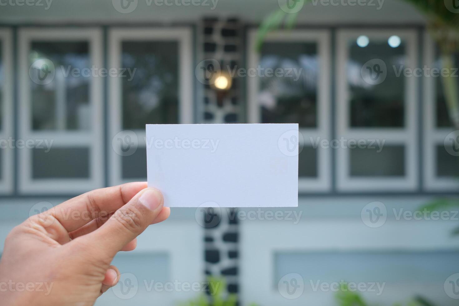 Hand holding a blank white card against a blurred background of a building. photo