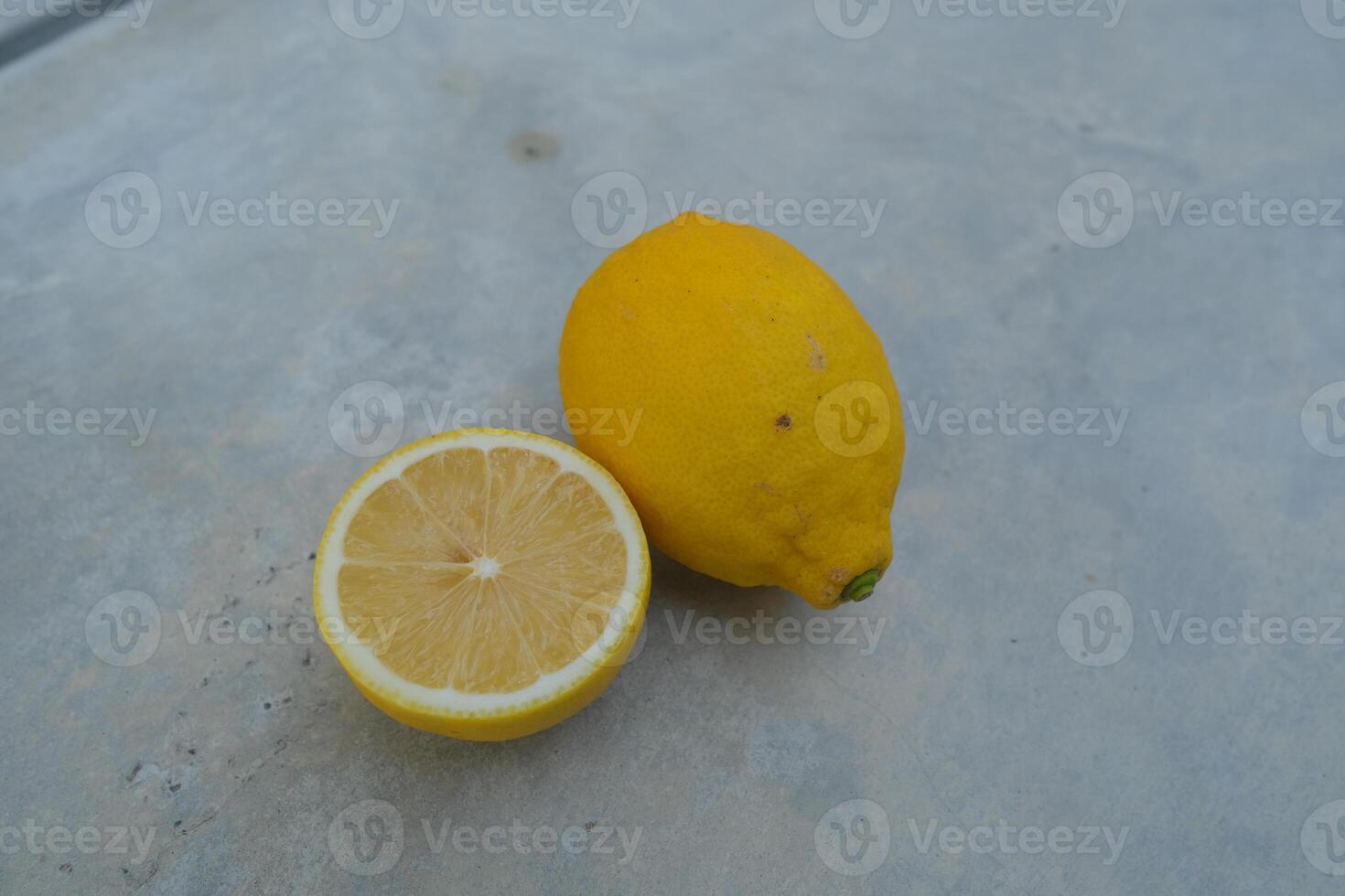 A whole lemon and a cut lemon slice on a grey surface. photo