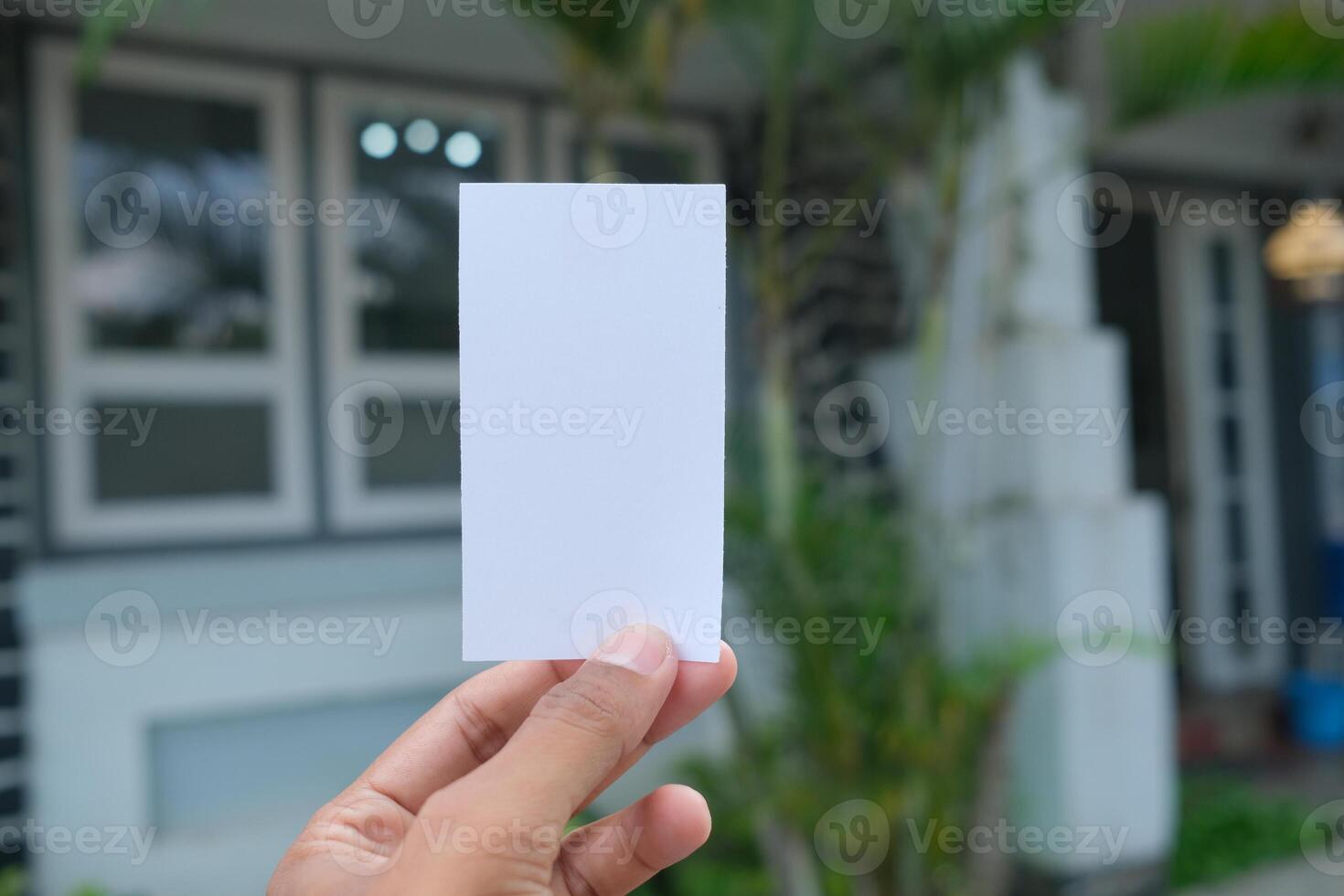 Hand holding blank white card, blurred house background. photo