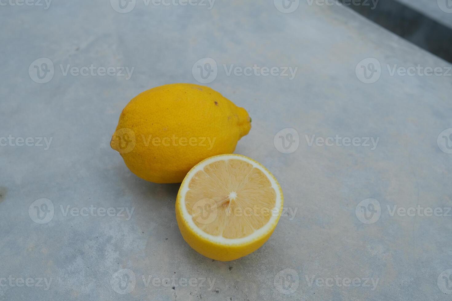 A whole lemon and a sliced lemon on a grey surface. photo