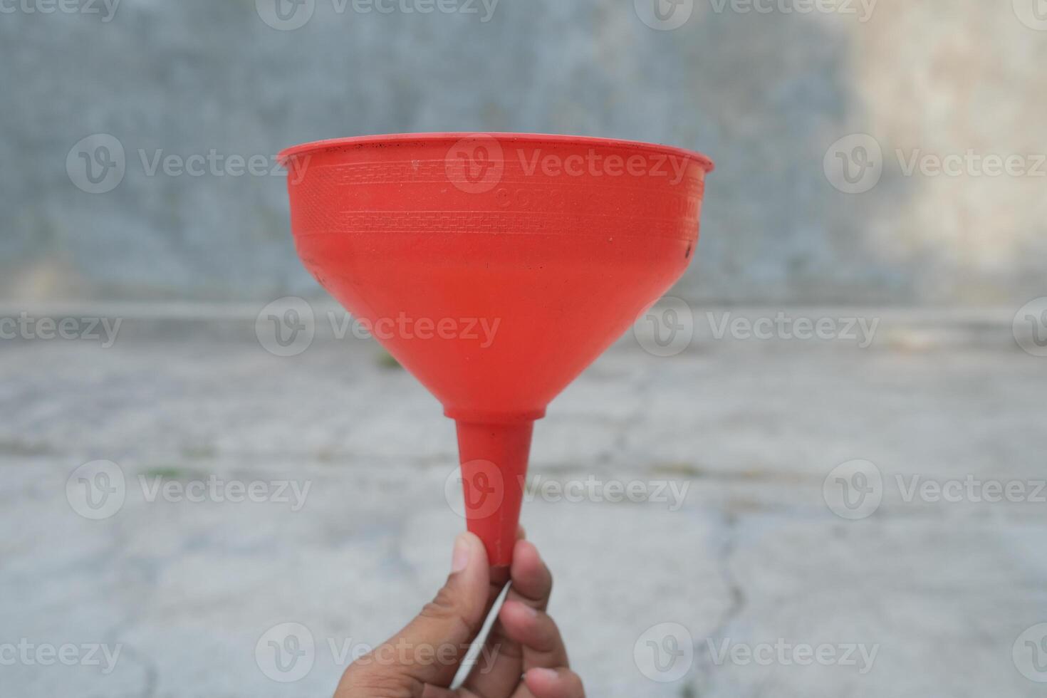 A hand holding a red plastic funnel. photo