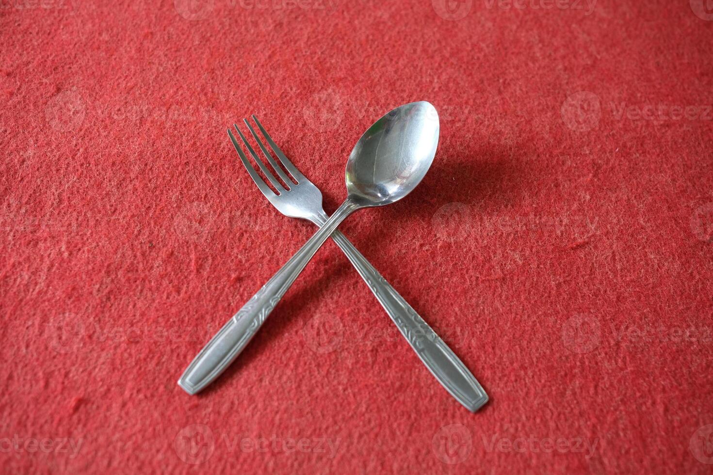 A fork and spoon crossed on a red surface. photo