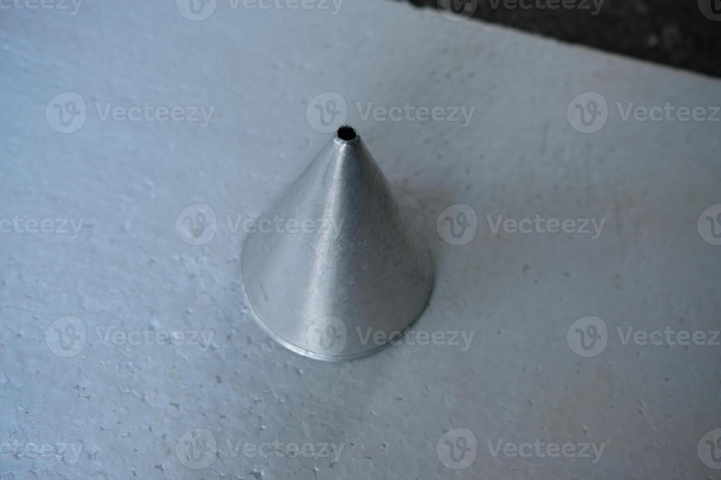 A single, metallic, cone-shaped mold sits on a white surface. photo