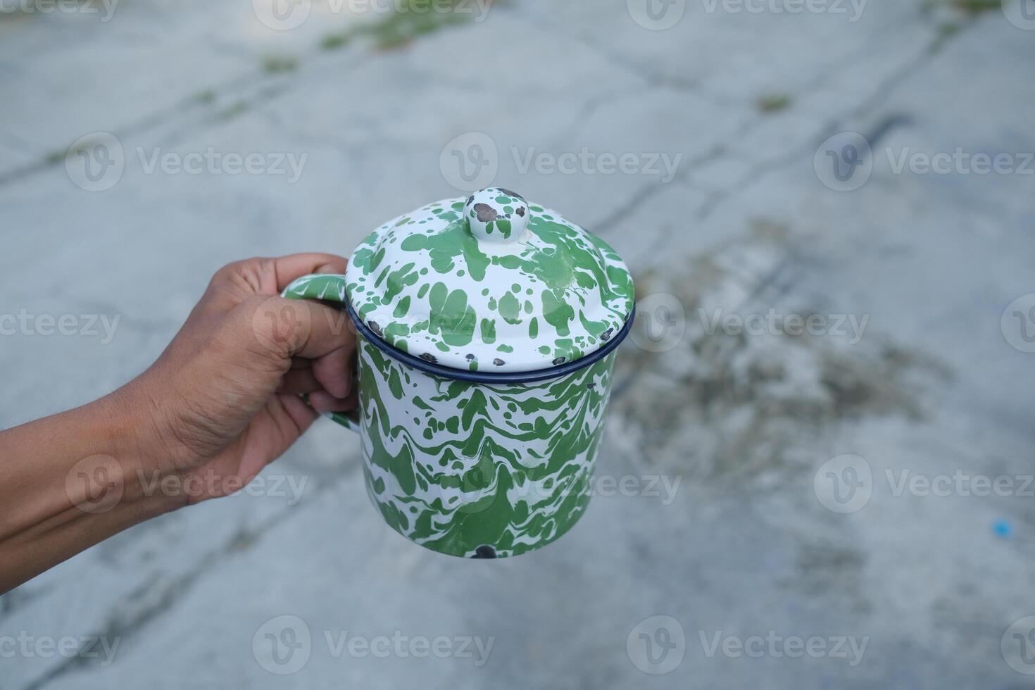 Hand holding a green and white patterned mug with a lid. photo