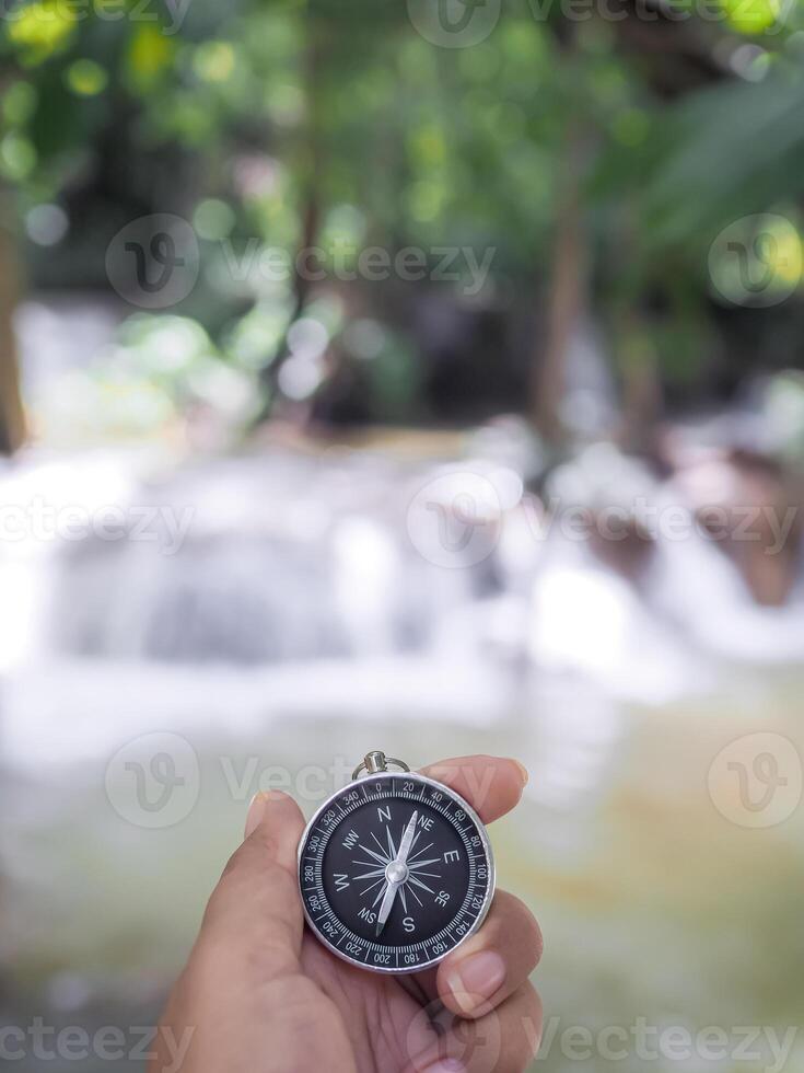 Close up of compass in woman hand with waterfall as background. The concept of world tourism day, Searching the right directions and Travel photo