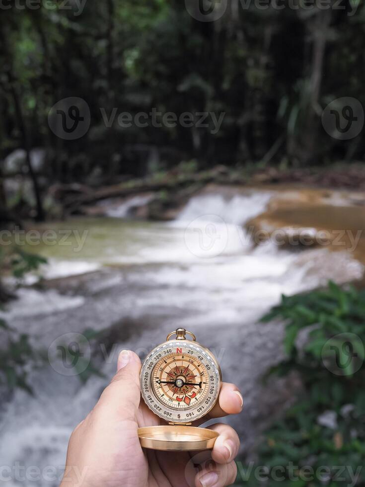 Close up of compass in woman hand with waterfall as background. The concept of world tourism day, Searching the right directions and Travel photo
