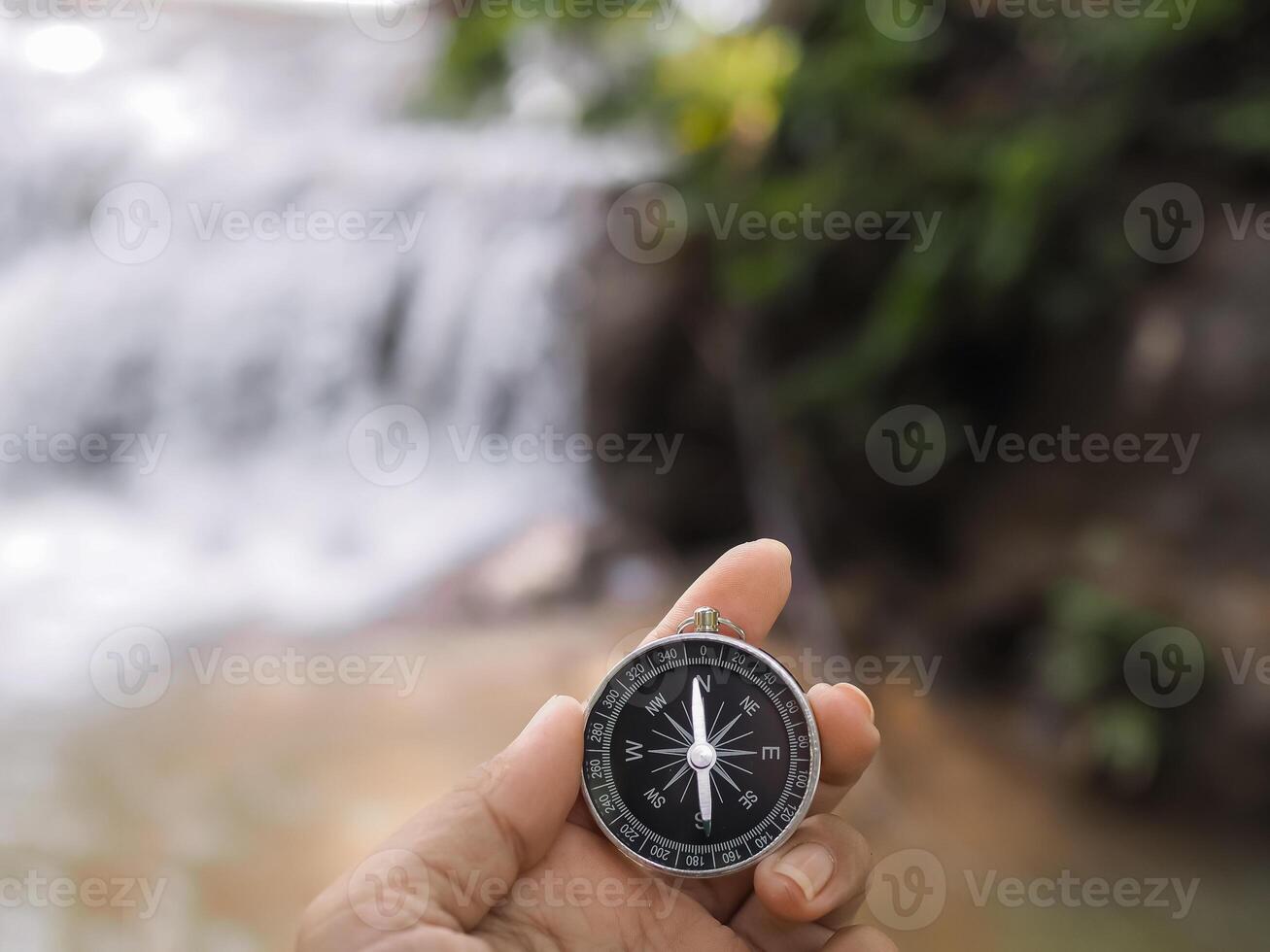 Close up of compass in woman hand with waterfall as background. The concept of world tourism day, Searching the right directions and Travel photo