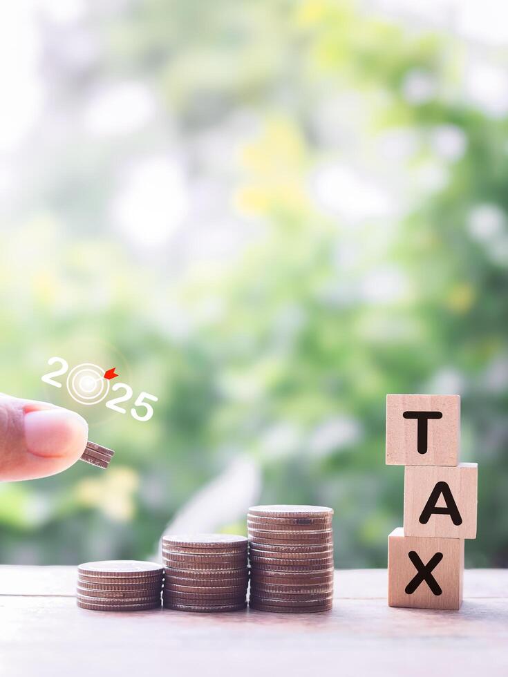 Close up hand putting coin into stack of coins and Wooden blocks with the word TAX. The concept about saving money and manage time to paying tax photo