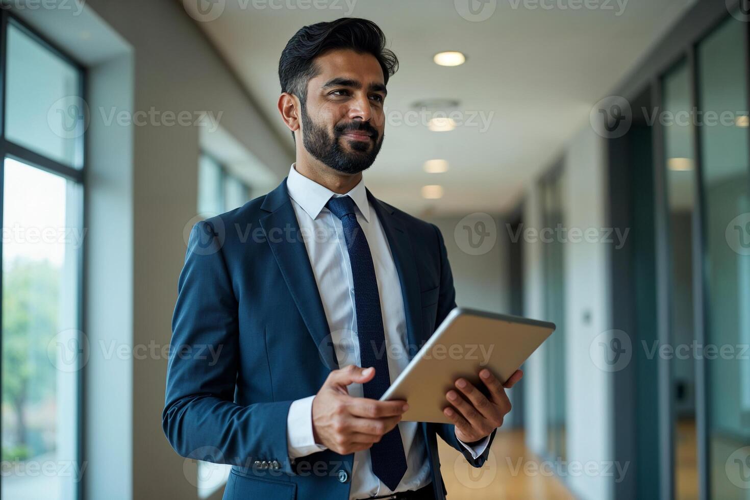 Confident Indian business man leader looking aside walking in office. Busy professional businessman going in hallway holding digital tablet thinking of work plan using tab computer. Authentic photo