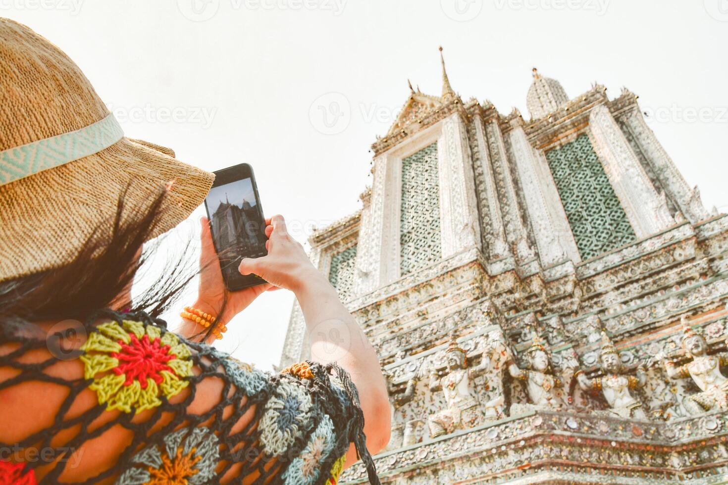 Close up woman tourist taking photo using mobile phone by beautiful Wat Arun temple in Bangkok, Thailand. Famous tourist destination content creator concept post social media