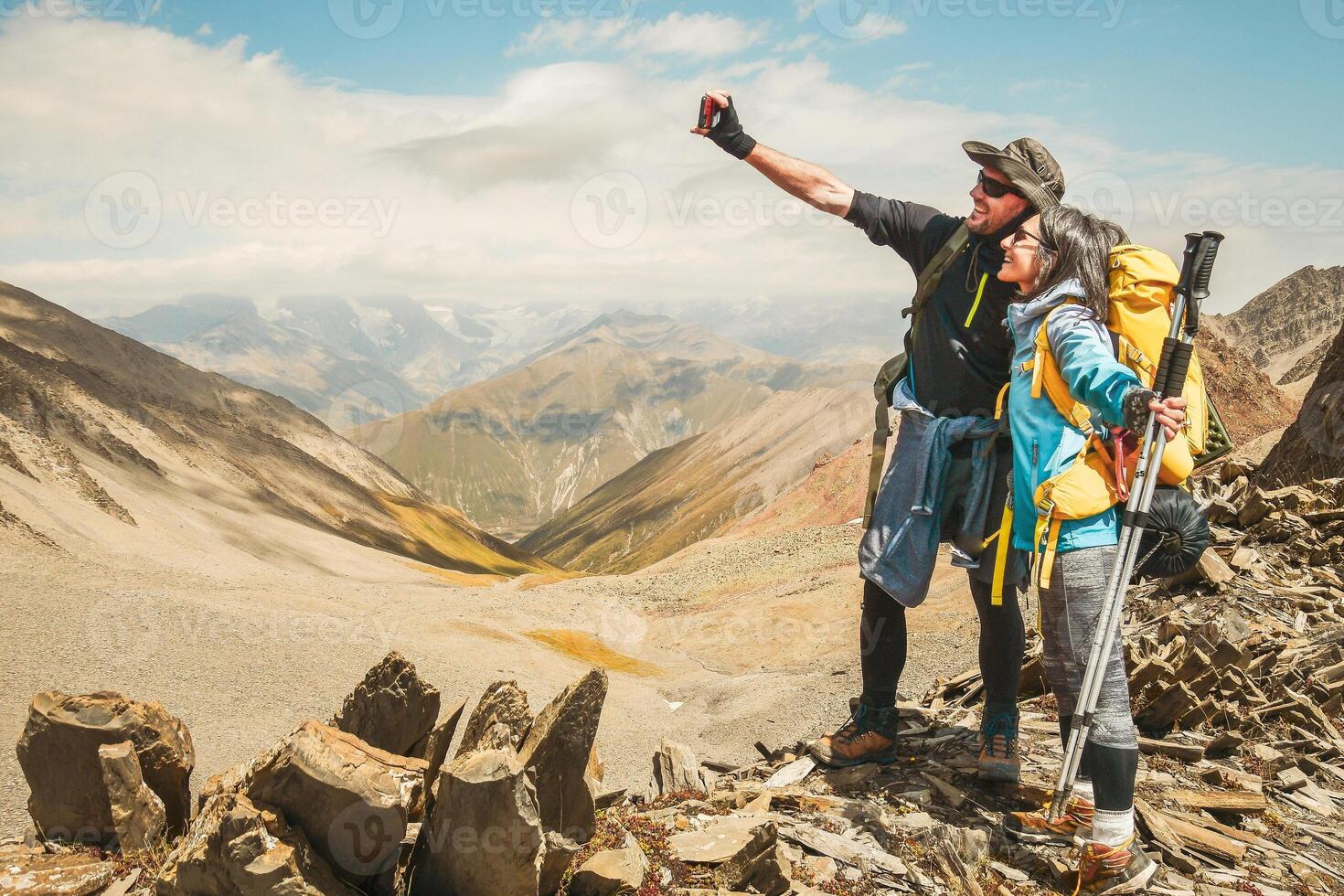 Close up young happy caucasian active millennial couple influencers take smartphone selfie while having fun on hiking trip outdoors reaching mountain peak destination photo