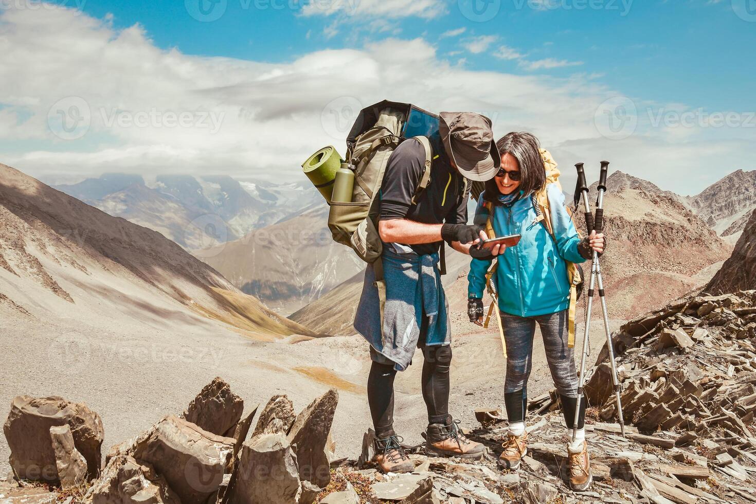 Attractive young Couple of hikers using a smartphone for orientation while out in mountains nature and wearing backpacks with camping gear. Trails treks being lost concept high in mountains photo