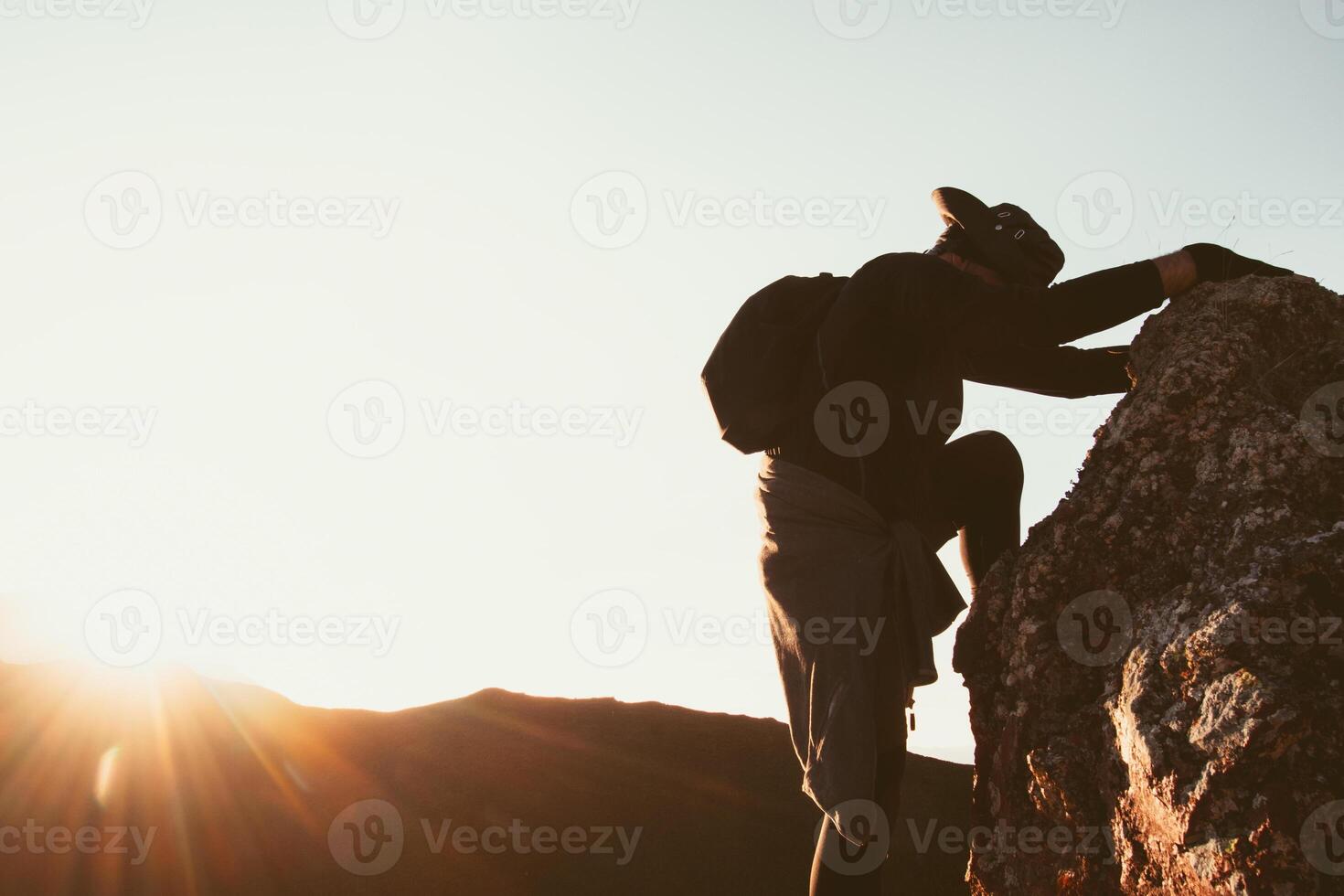 Fit young determined caucasian man climbing to top of mountain take a break rest on way up. Travel, hard work reaching goals concept.Tired look at sunset sunflare sunburst trust in God concept photo