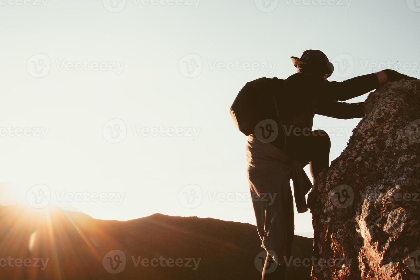 Fit young determined caucasian man climbing to top of mountain take a break rest on way up. Travel, hard work reaching goals concept.Tired look at sunset sunflare sunburst trust in God concept photo