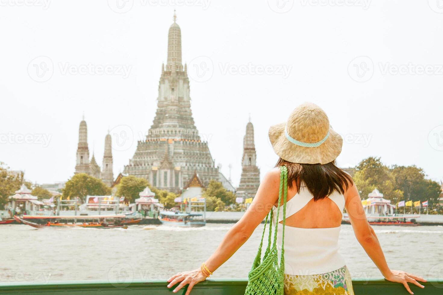 Young pretty woman tourist on viewpoint enjoying panorama looking at Wat Arun - Buddhist temple in the Bangkok Yai district of Bangkok, Thailand. Thonburi on west bank of the Chao Phraya River photo