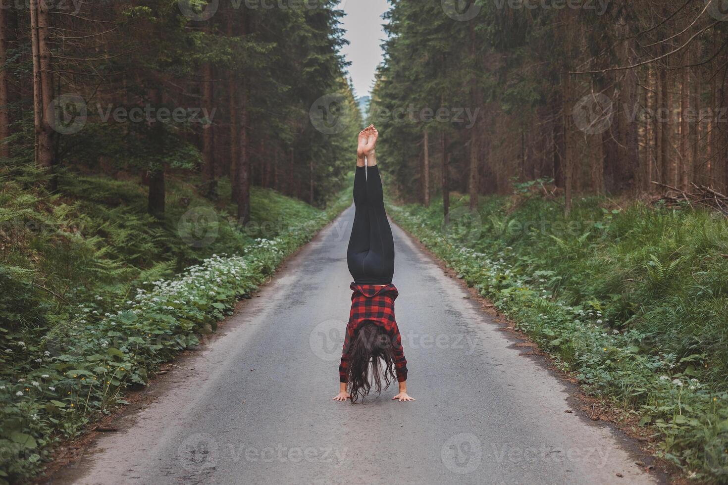 Acrobatic woman in black leggings and plaid shirt performs a cartwheel on a forest path in the middle of a deep forest. Coordination and agility training photo