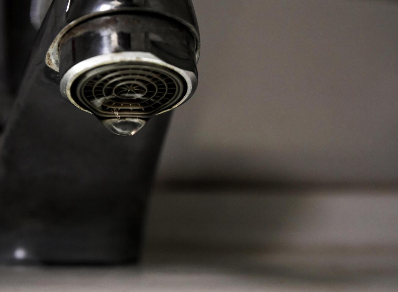 Leaking water drops from old rust and stained faucet photo