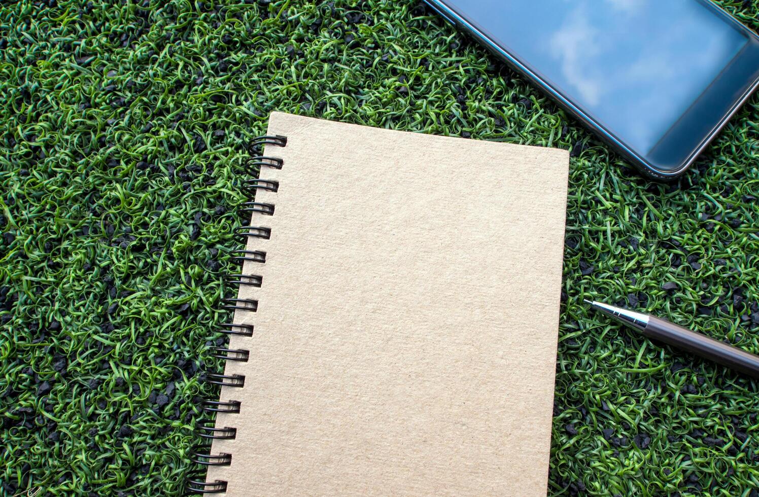 Kraft paper spiral notebook with pen on the Artificial turf photo