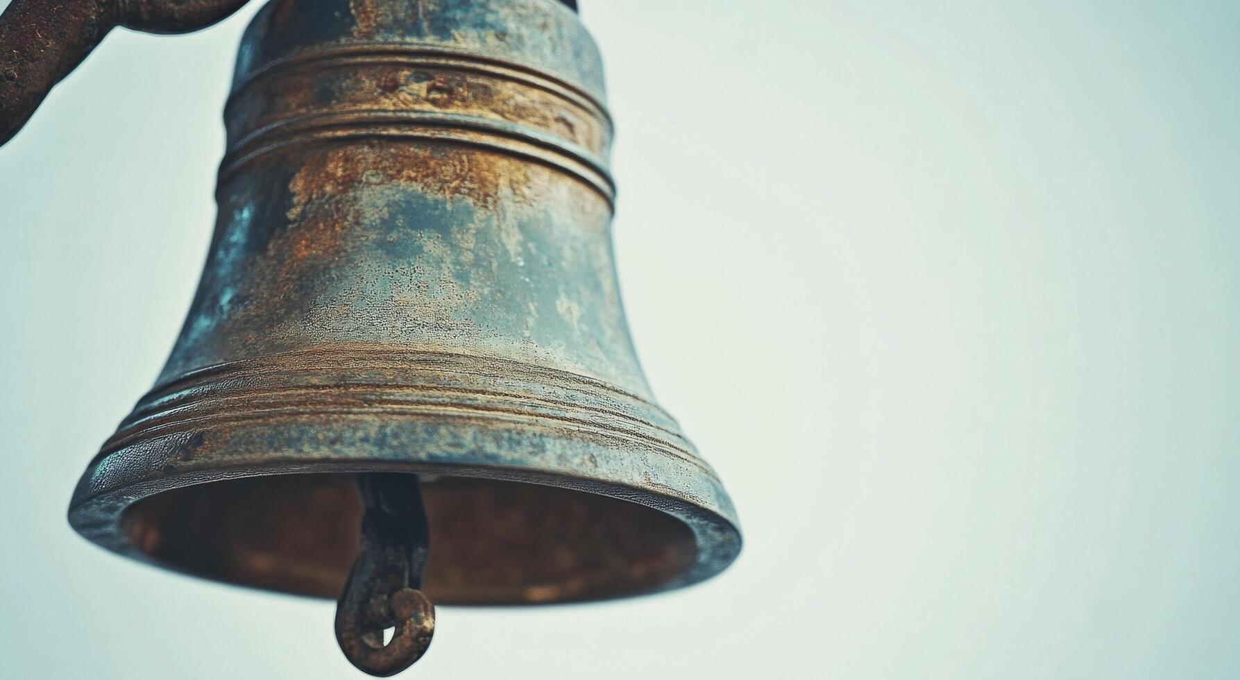 Rustic bronze bell hanging from a branch with blurred background of autumn leaves during daylight photo