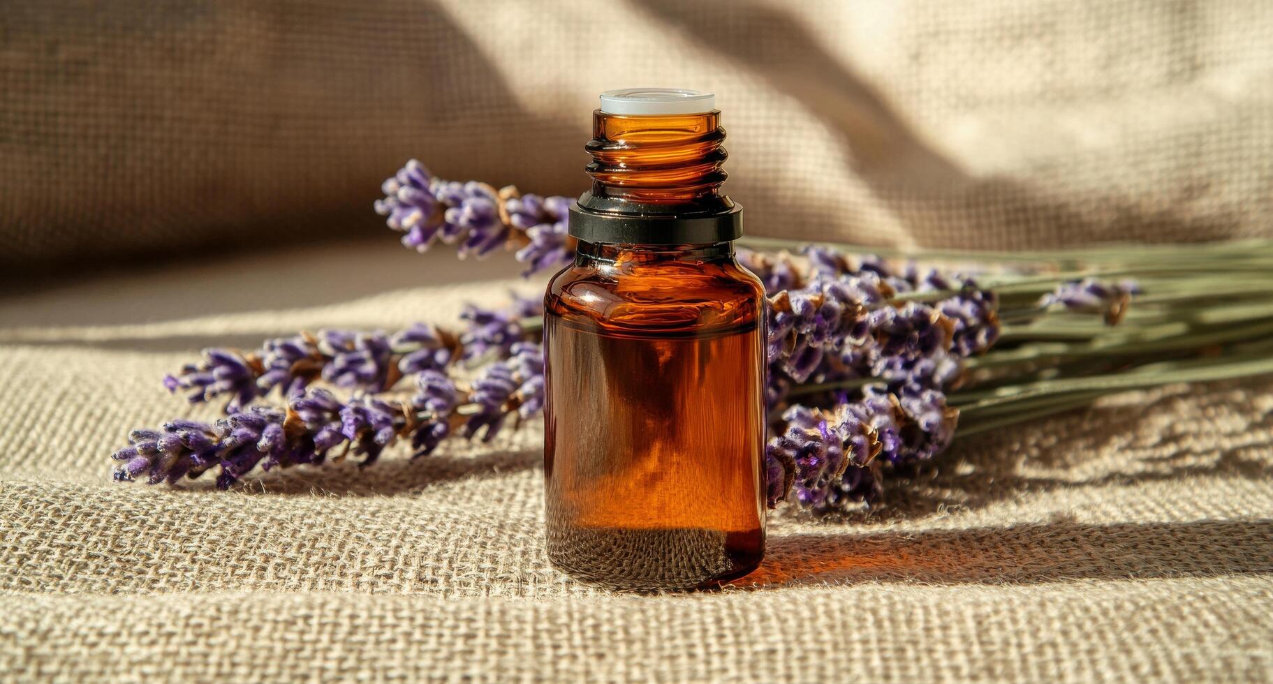 Lavender essential oil bottle rests beside fresh lavender flowers on a textured fabric background photo