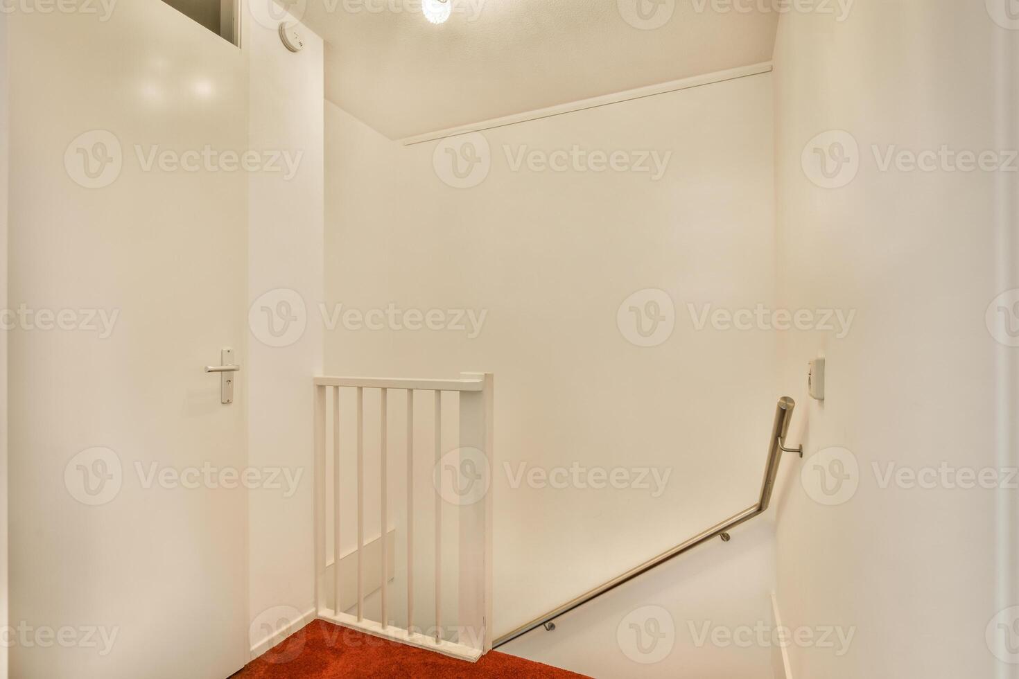 A white hallway with a red carpet and a red door photo