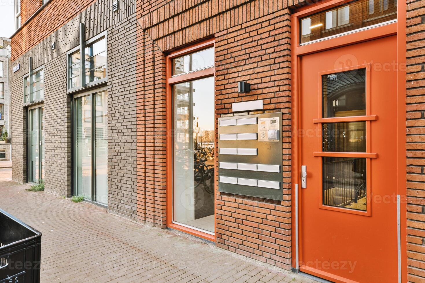 A brick building with a red door and a trash can photo