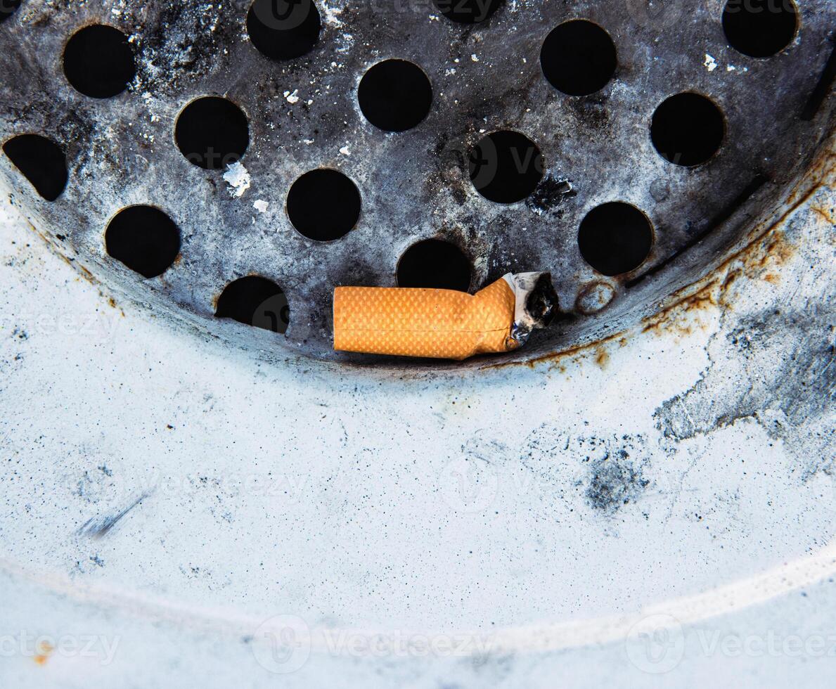 Closeup of a discarded cigarette butt stuck in a rusted metal grate of garbage bin. Nonsmoking, smoking harm, urban pollution, healthy and unhealthy lifestyle, littering, environmental concept. photo