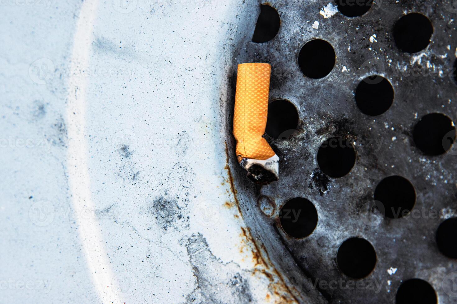 Closeup of a discarded cigarette butt stuck in a rusted metal grate of garbage bin. Nonsmoking, smoking harm, urban pollution, healthy and unhealthy lifestyle, littering, environmental concept. photo