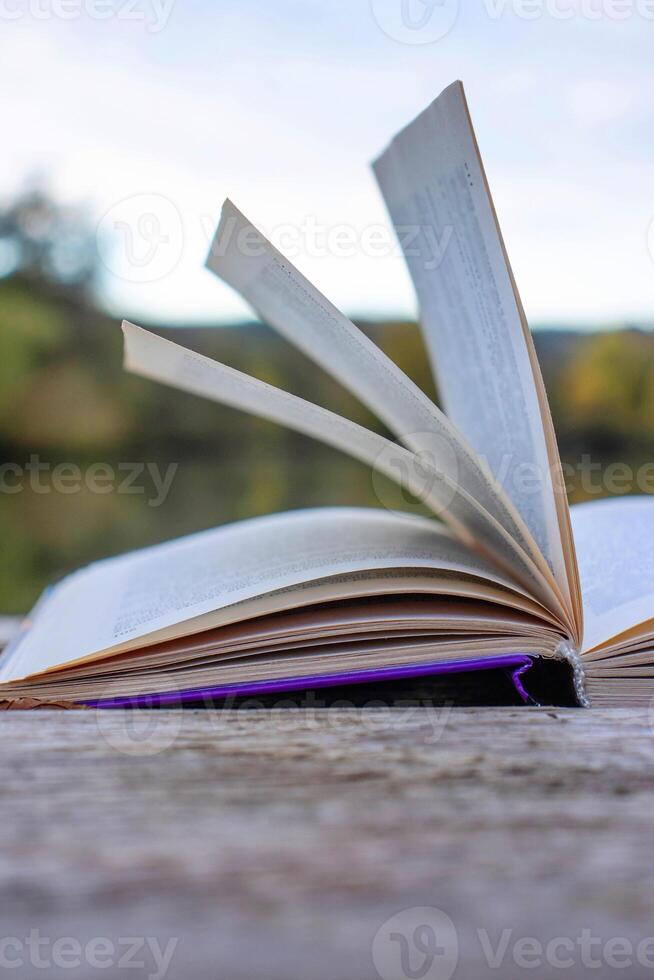 Open book with pages flipping in the wind. Reading on the lake wooden dock on autumn day. Learning enjoying tranquility of nature. Peaceful outdoor environment. Selective focus. Blurred background. photo