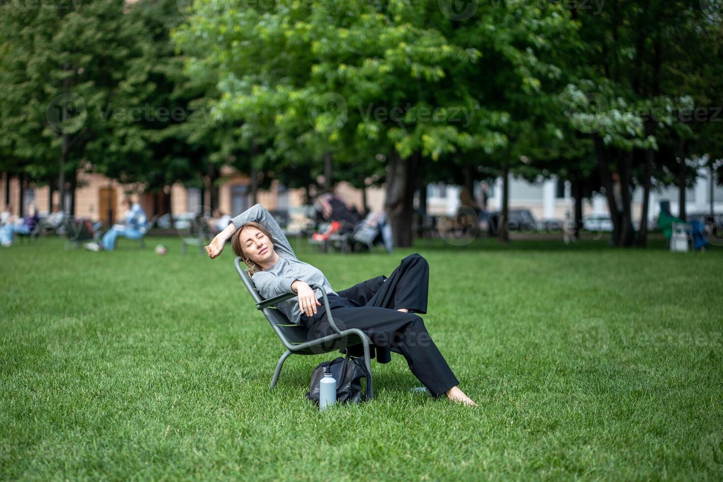 Relaxed woman dozing napping, sitting on folding chair on lawn in nature park outside outdoors photo