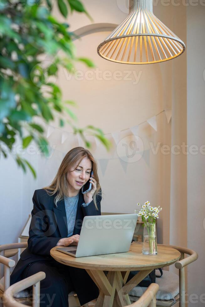 Smiling businesswoman working with laptop in cafe at table, talking on phone with colleague, friend. photo