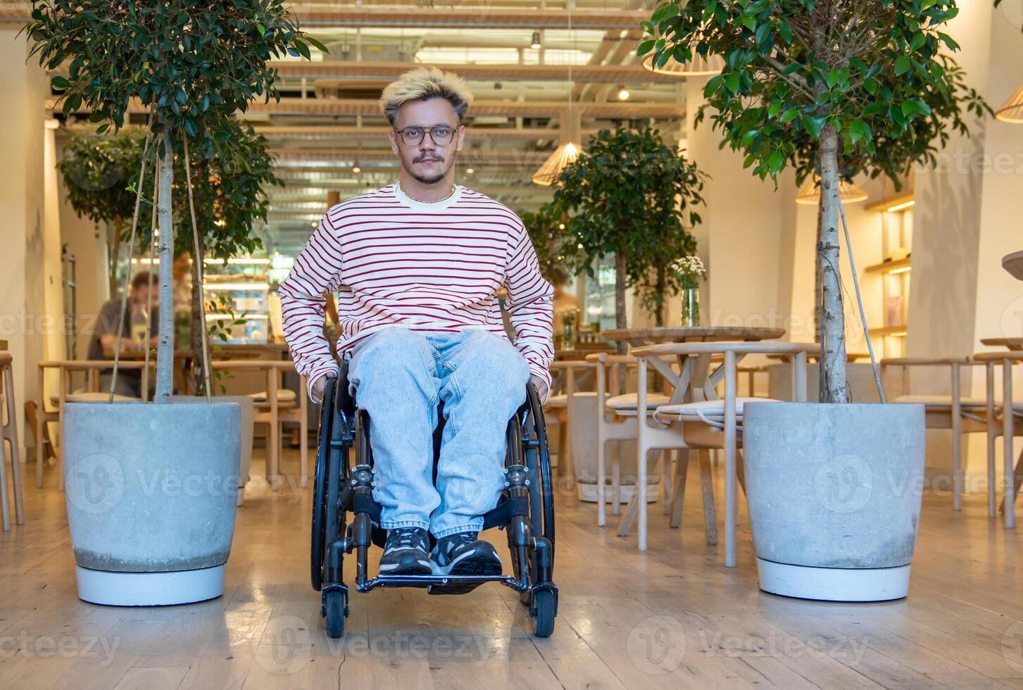 relajado confidente discapacitado hombre en silla de ruedas dejando cafetería, mira a cámara. accesible público espacio foto