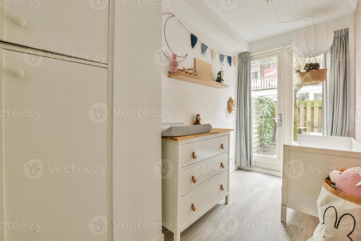 A small nursery room with a white dresser and a wooden floor photo