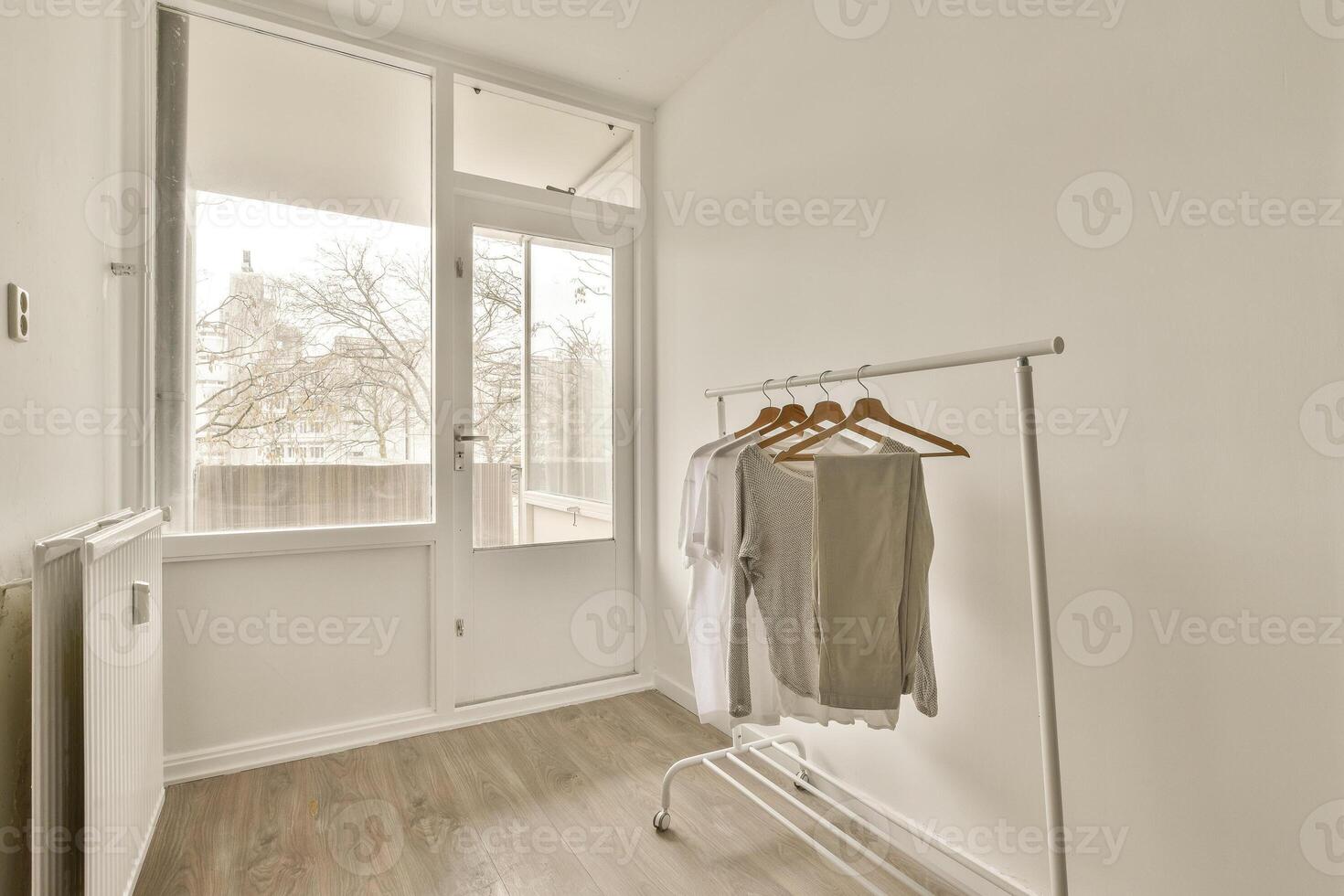 A white room with a clothes rack and a window photo