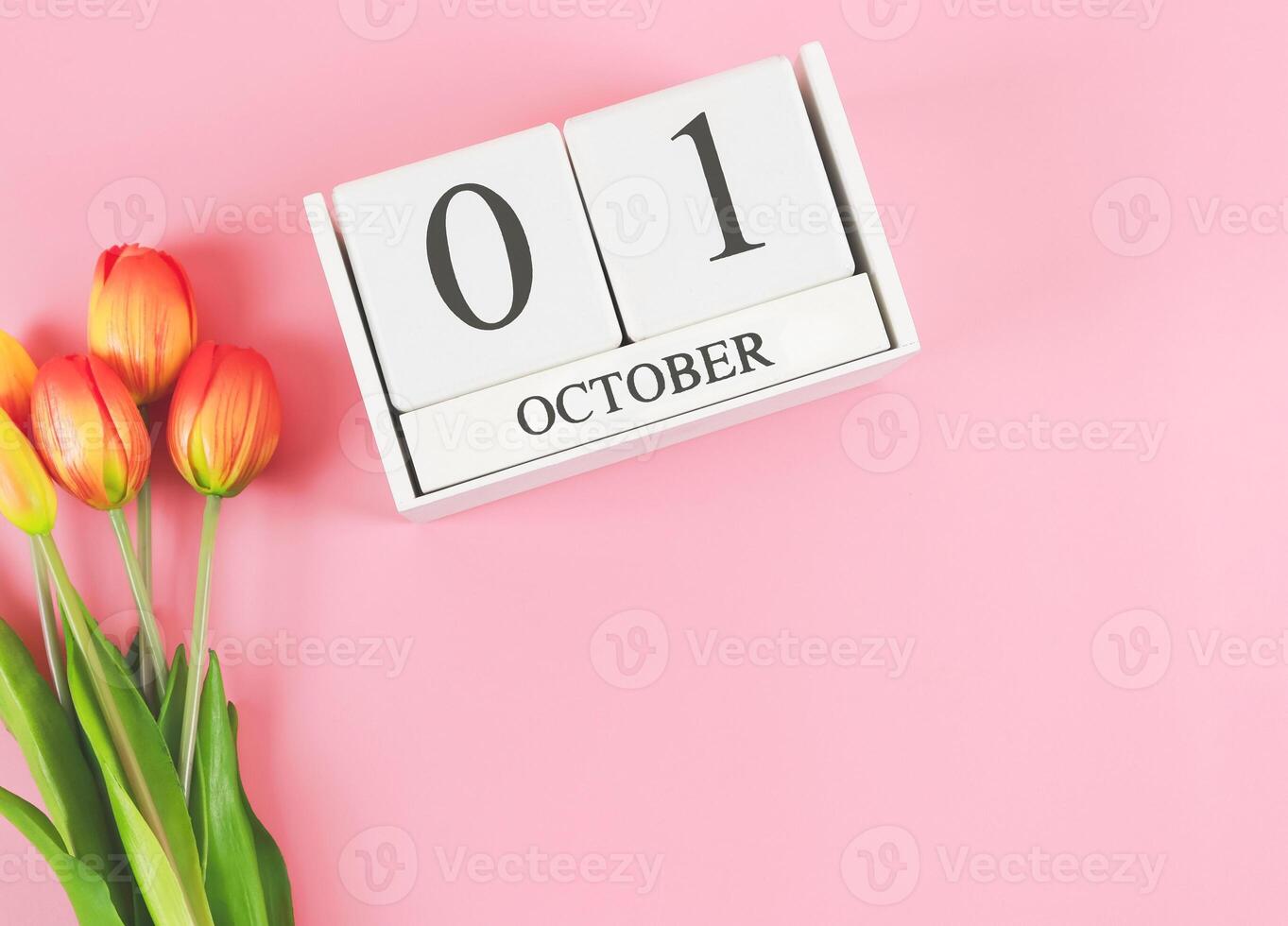 flat lay of wooden calendar with date October 01 on pink background with orange and yellow tulips, copy space. photo
