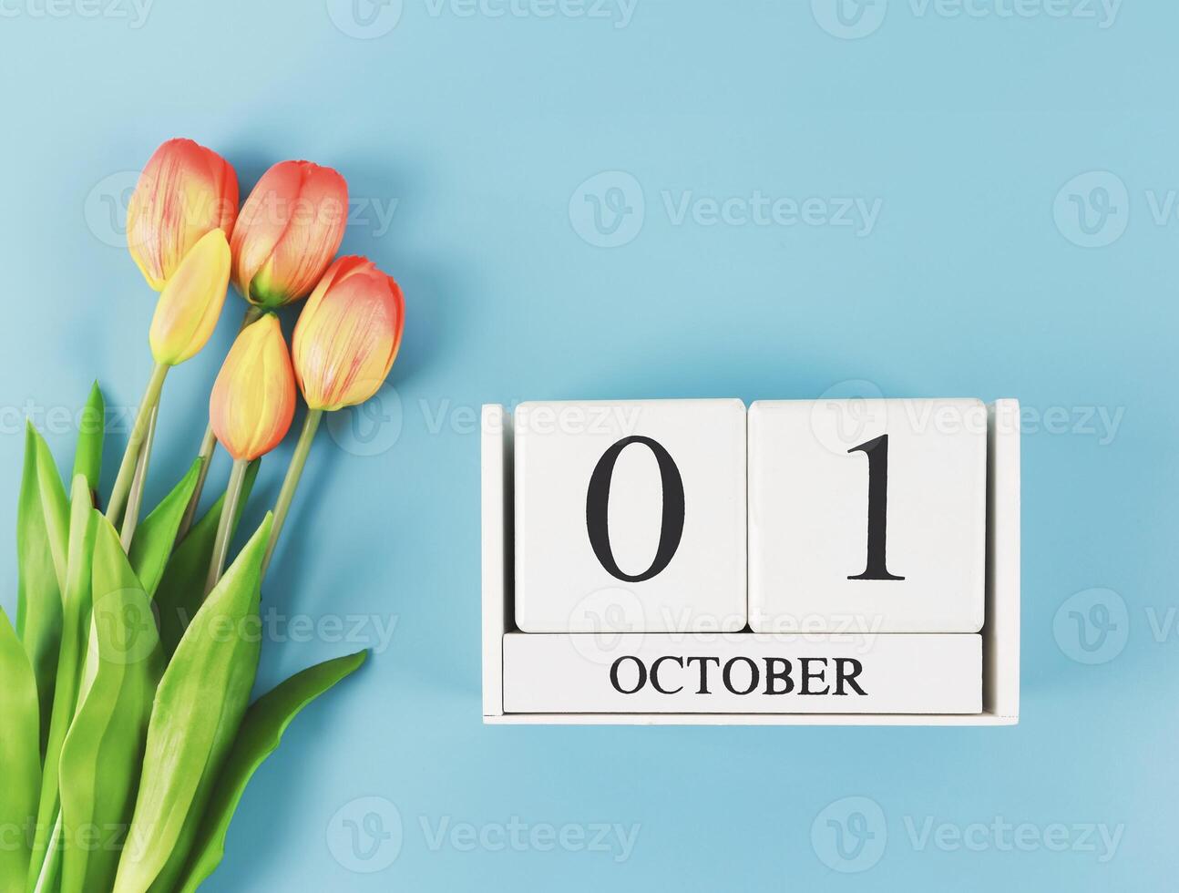 flat lay of wooden calendar with date October 01 on blue background with orange and yellow tulips, copy space. photo