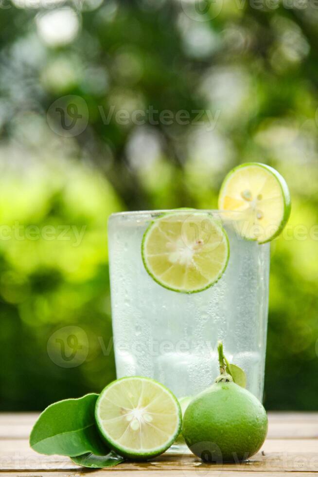 Glass of cold water with fresh lime slices, healthy drink of lime with lime slices placed on wooden table and natural background photo