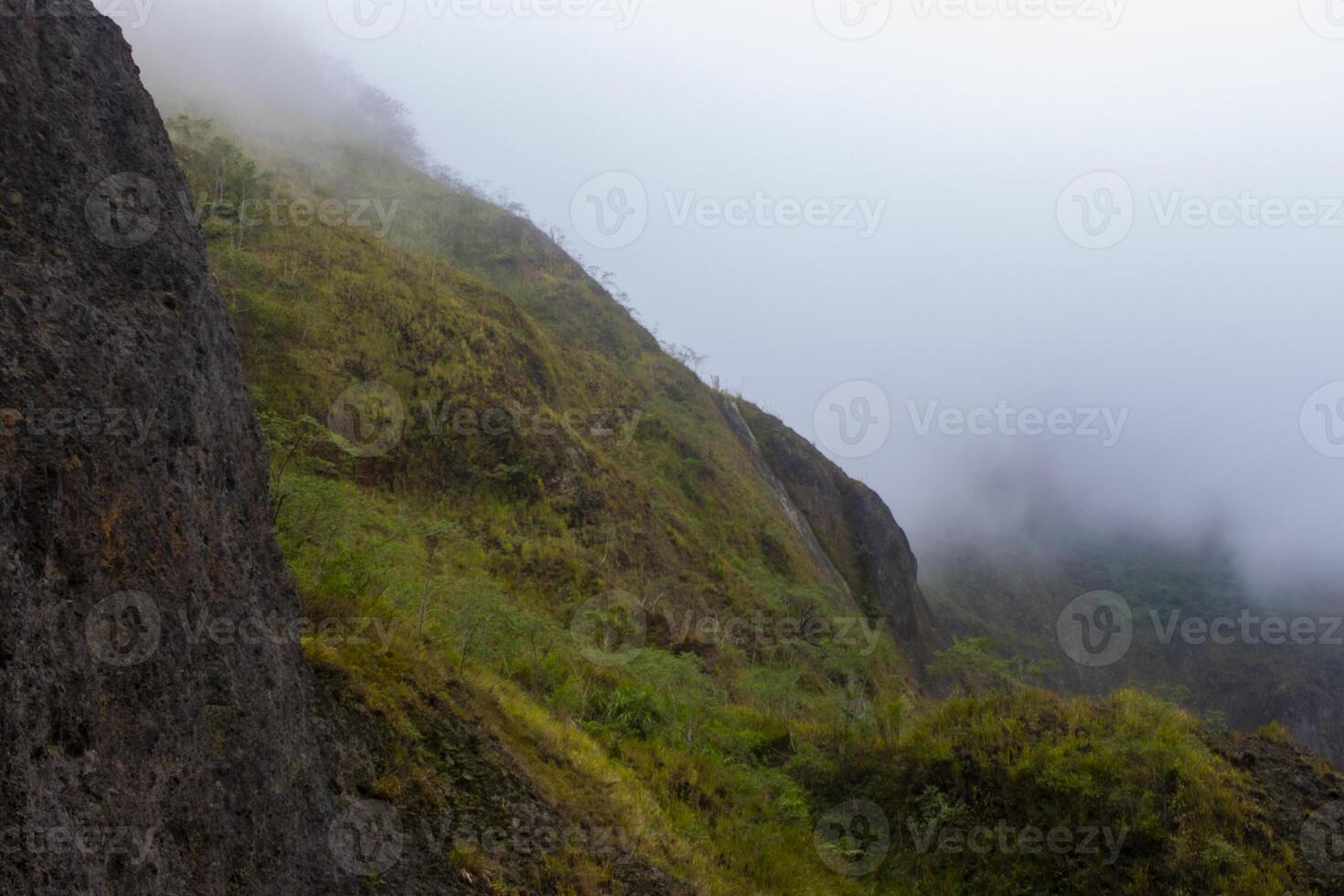 The slopes of Mount Kelud with green bushes and trees, and thick fog hanging above it. One of active volcanoes in East Java, Indonesia. photo