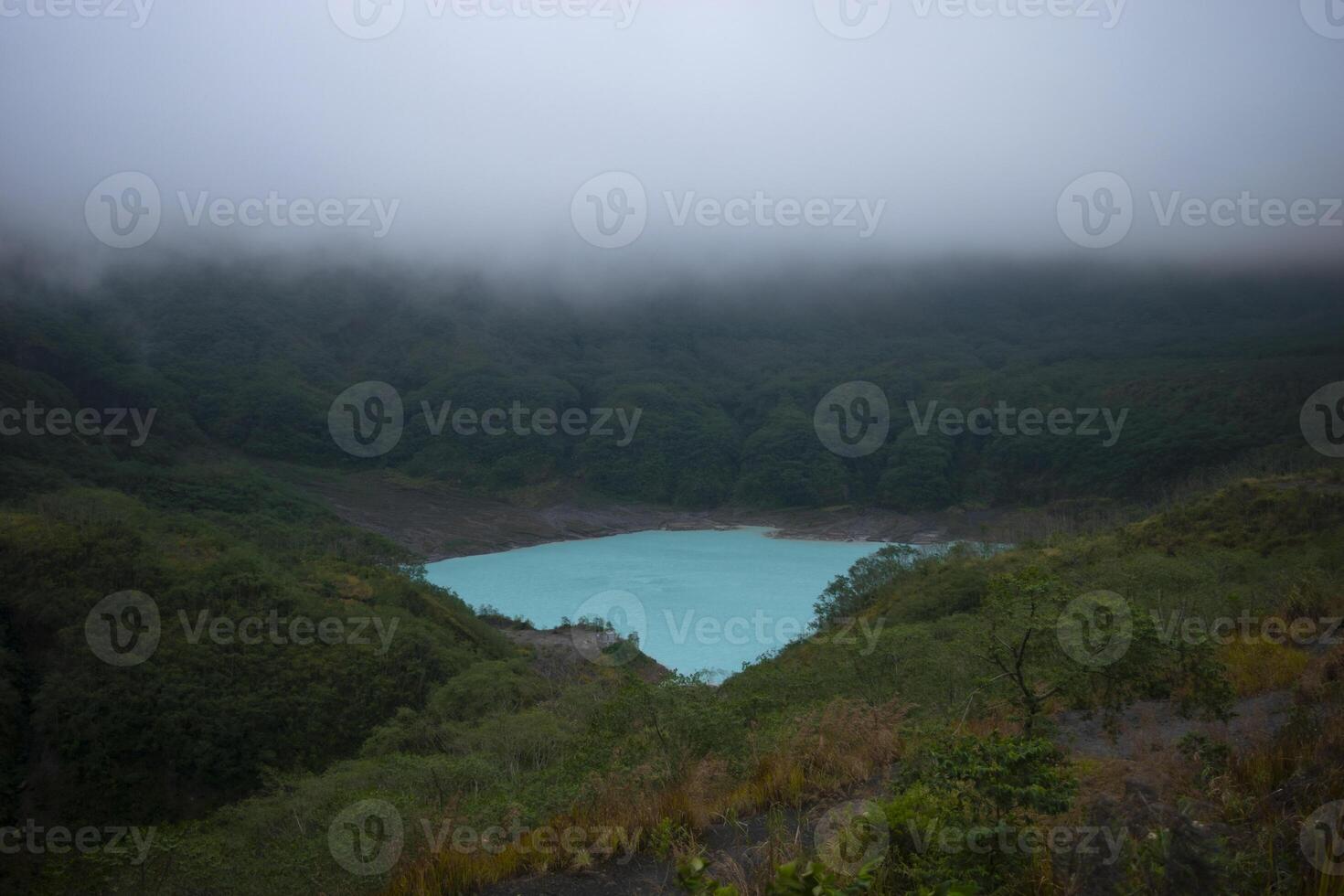 Beautiful view of the crater of Mount Kelud when it is inactive with turquoise lake water and thick fog above it. photo