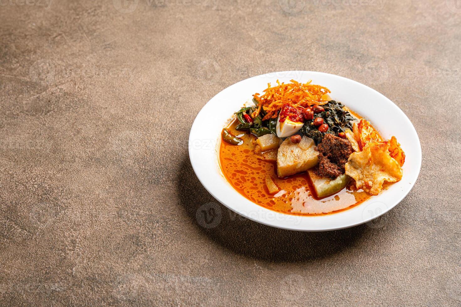Lontong sayur or vegetable rice cake is an Indonesian traditional rice dish made of pieces of lontong served in coconut milk soup with shredded chayote, tempeh, tofu, hard-boiled egg, sambal, rendang photo