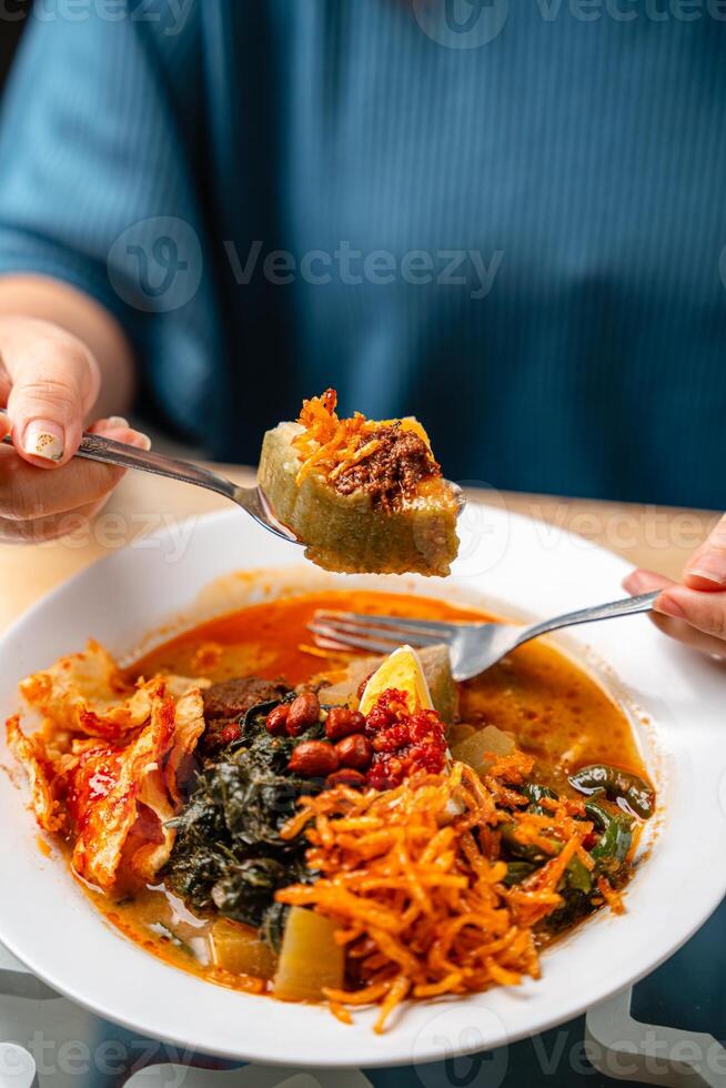 Lontong sayur or vegetable rice cake is an Indonesian traditional rice dish made of pieces of lontong served in coconut milk soup with shredded chayote, tempeh, tofu, hard-boiled egg, sambal, rendang photo