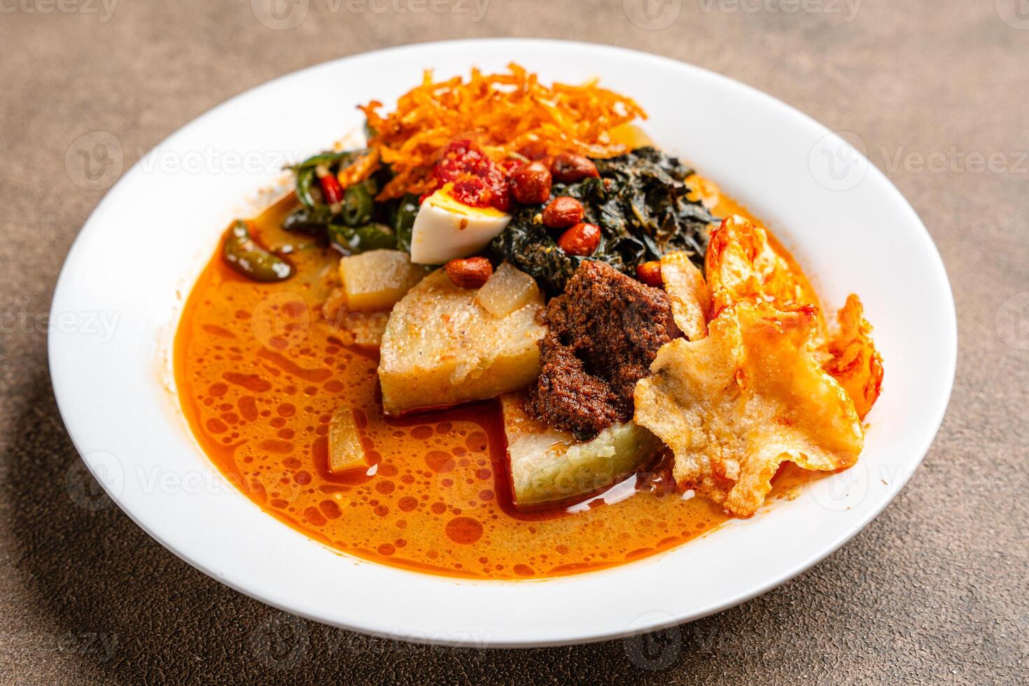 Lontong sayur or vegetable rice cake is an Indonesian traditional rice dish made of pieces of lontong served in coconut milk soup with shredded chayote, tempeh, tofu, hard-boiled egg, sambal, rendang photo