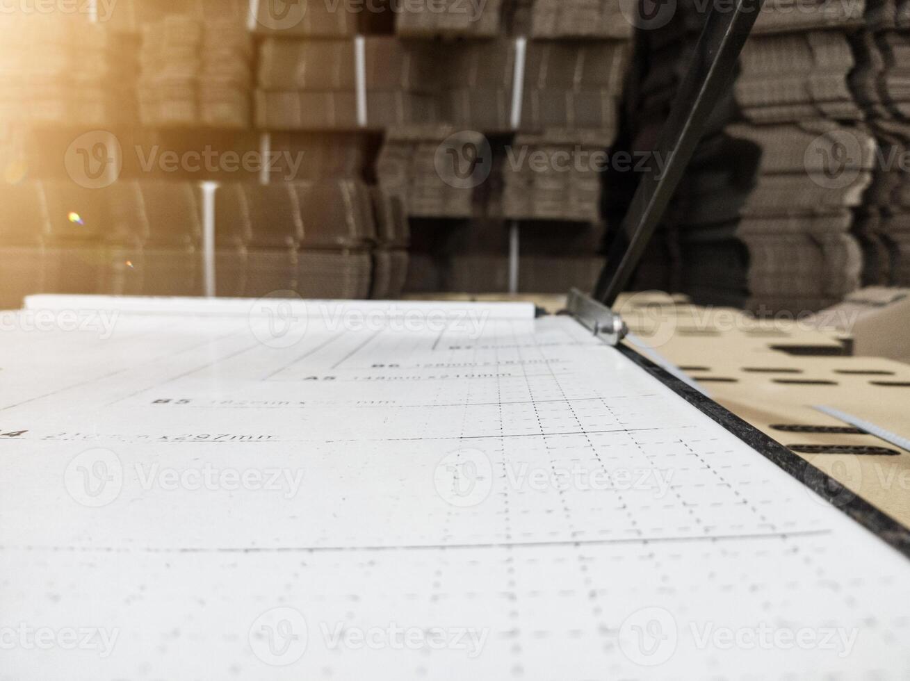 Close up of the paper cutter with a background of a pile of brown cardboard and shiny light. photo