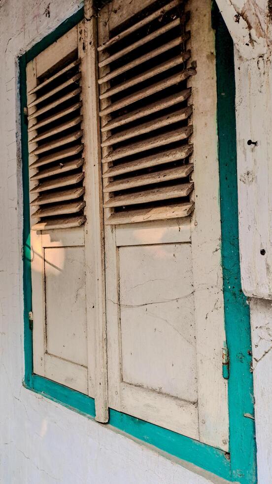 A pair of old, wooden window shutters painted in light beige with a teal frame. photo