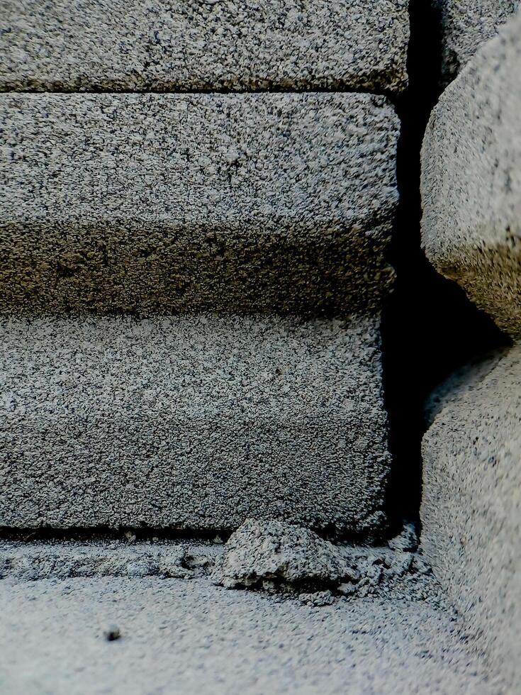 weathered concrete surface, showcasing the rough texture, cracks, and shadows created by its uneven surface. photo
